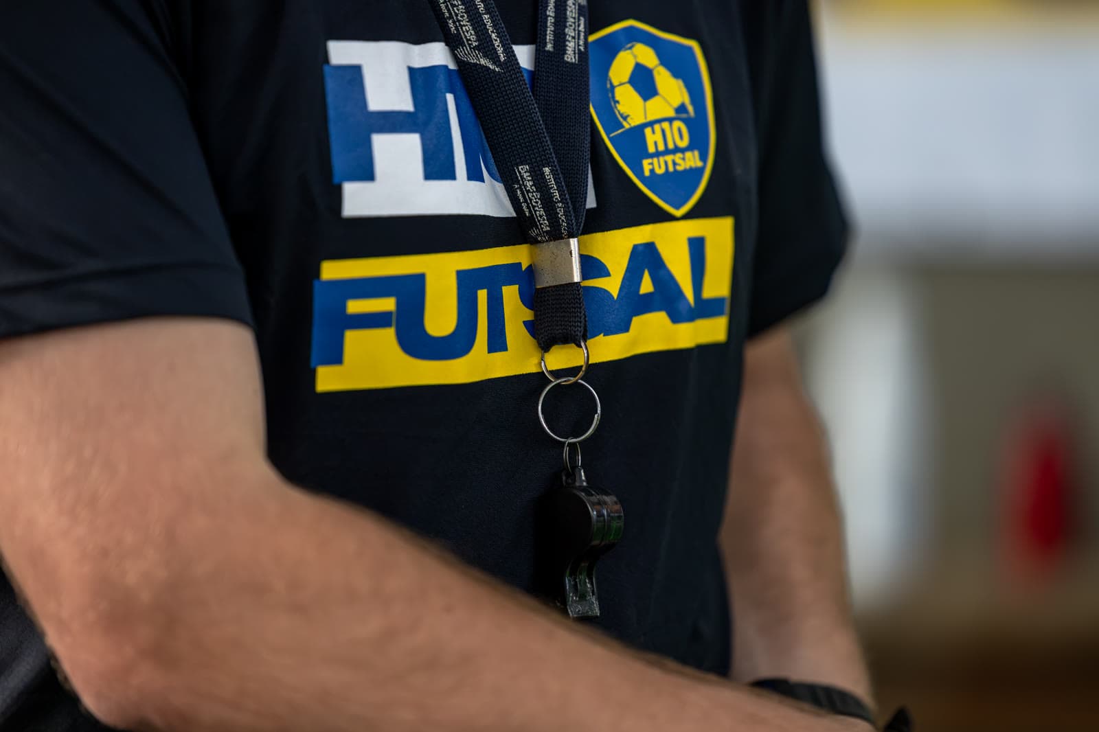 Detalhe do apito e do crachá no peito de um treinador de camiseta H10 Futsal