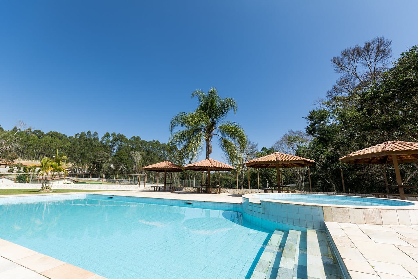 Piscina descoberta com quiosques de sapê e coqueiros em volta