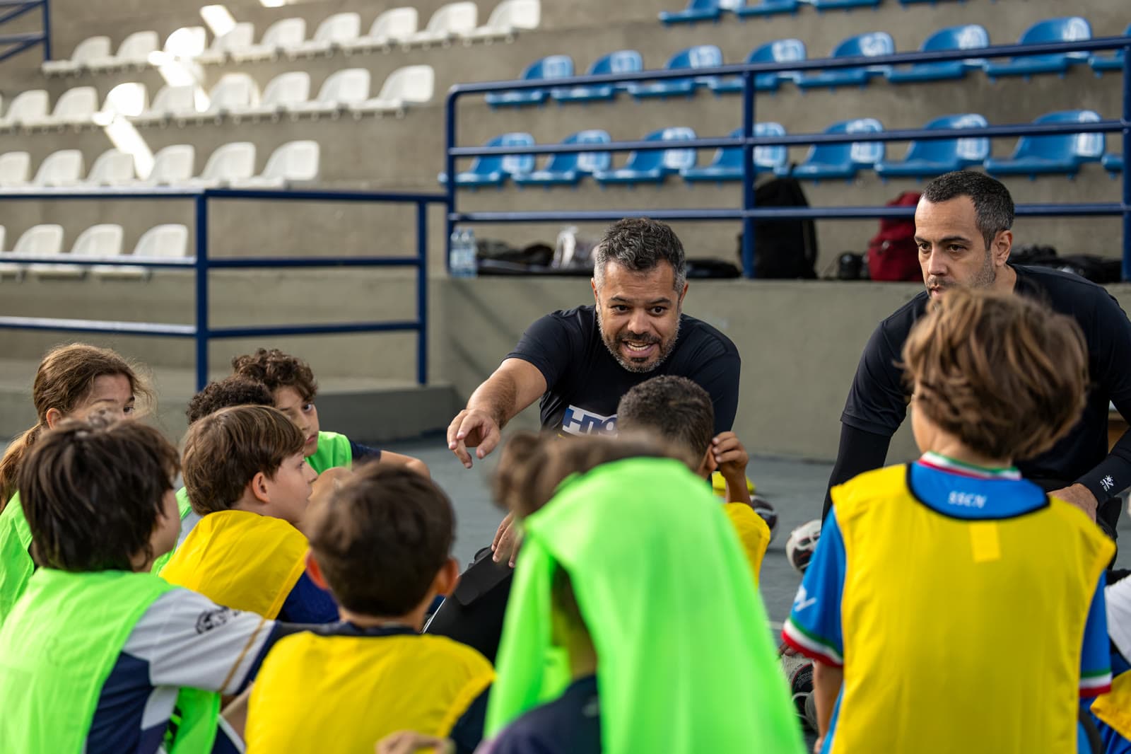 Treinador explicando o formato de jogo a uma roda de crianças em quadra