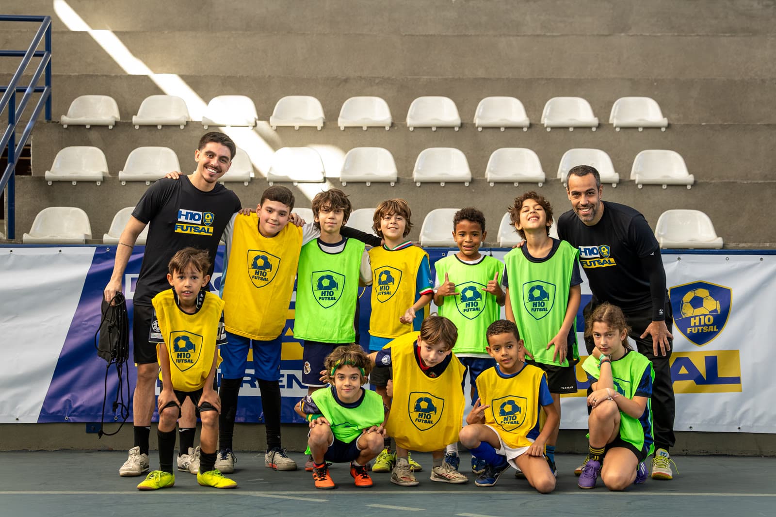 Dois treinadores posando com atletas na arquibancada